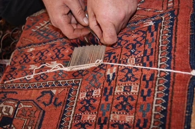 Les mains de l'artisan retissent le velours nœud par nœud sur la chaîne reconstituée d'un tapis rouge