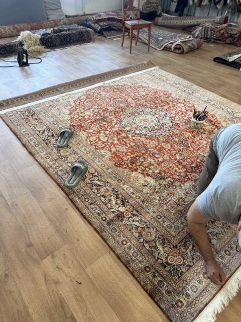 Artisan préparant un grand tapis persan pour la rénovation de ses couleurs dans l'atelier